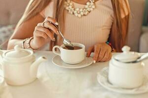 mujer con té. manos sostener un cucharilla. blanco vajilla en el mesa. foto