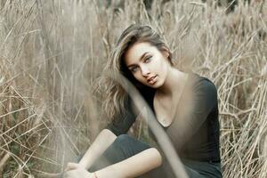 hermosa joven niña en un negro camiseta sentado en el seco césped. foto