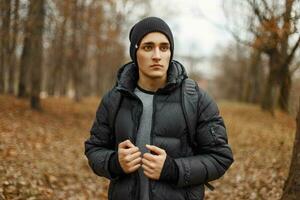 hermoso joven hombre en invierno ropa con un mochila en el antecedentes de un otoño bosque. foto