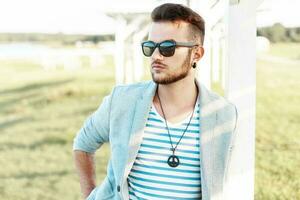 Handsome hipster man in sunglasses with a beard in a trendy suit and shirt on the beach. photo