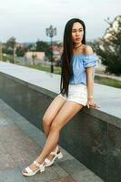 Beautiful young girl in stylish blue blouse and white shorts on a background of the city photo