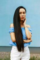 Pretty beautiful asian woman in a fashionable summer clothes standing near a blue wall photo