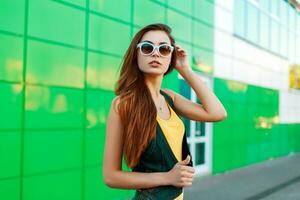 Beautiful young woman in bright stylish clothes stands near modern building. photo