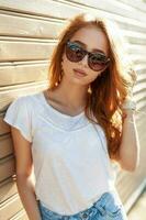 Beautiful young woman in sunglasses and white shirt leaned against on the wooden wall. photo