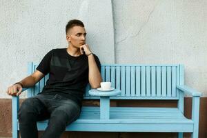 Handsome lonely man sits alone on a bench and drink coffee photo