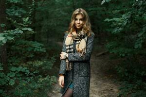 Beautiful girl in a coat and scarf in a dark forest photo