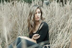 Beautiful young woman sitting in the dry grass. Wheat field photo