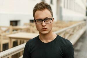 Handsome young man with glasses in a black shirt standing on the street. photo