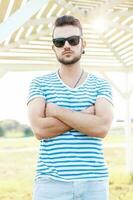 hermoso hombre con un barba en un verano camisa y Gafas de sol en pie en el playa en un soleado día. foto