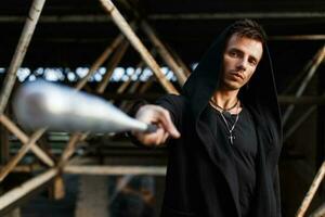 Serious man in black clothes with a hood holds a bat. photo