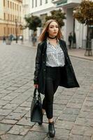 Young beautiful woman in autumn coat with stylish bag, shoes, striped blouse on the street photo