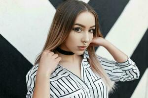 Young beautiful model girl in striped blouse with a pierced nose near a white wall with black stripes photo