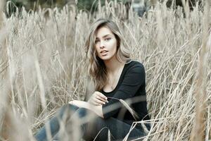 Pretty young woman sitting in the dry grass, photo