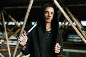 Angry man in black clothes holding a bat on the background of metal pipes photo