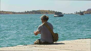 Traveler Man Capturing Ocean View With Cell Phone Sitting On Wooden Pier video