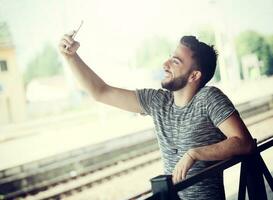 joven hombre a el tren estación toma un autofoto foto