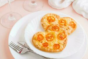 Two fresh pizzas in the shape of a heart on plates on a pink background. Valentine's Day. Close-up photo