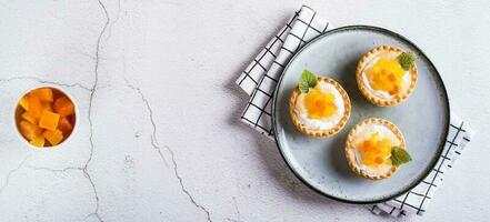 Appetizing tartlet with whipped cream, canned fruit and mint on a plate top view web banner photo
