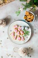 Freshly baked Christmas cookies with pink icing on a plate on a decorated table. Festive treat. Top and vertical view. Close-up photo
