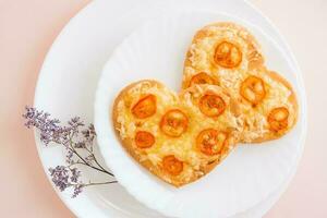 dos Fresco pizzas en el forma de un corazón en platos en un rosado antecedentes. San Valentín día. de cerca. parte superior ver foto