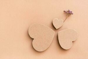 Family concept. Three cardboard hearts - dad, mom and baby with a dry flower in a circle on a beige background. Top view. Copy space photo
