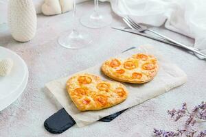 dos corazón conformado listo para comer pizzas en papel en conjunto mesa para San Valentín día celebracion. de cerca foto