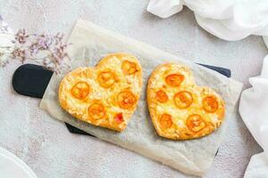 Two heart shaped ready-to-eat pizzas on paper on set table for valentine's day celebration. Close-up. Top view photo