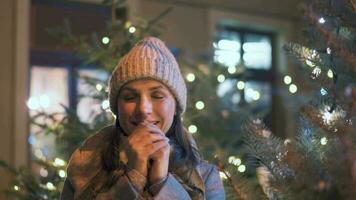 portrait de une content femme contre le toile de fond de Noël décorations. elle frotte sa mains, en gardant leur chaud de le froid. Noël et Nouveau année vacances concept video