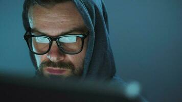 manlig hacker i de huva och glasögon arbetssätt på en dator i en mörk kontor rum. Cyber brott begrepp video