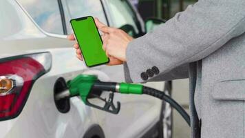 Woman uses a mobile application in a smartphone to pay for refuelling a car. Smartphone with a green screen. Chroma key video