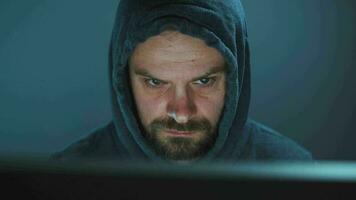 Male hacker in the hood working on a computer in a dark office room video