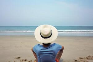 espalda ver de un hombre vistiendo un sombrero sentado en un playa. ai generado foto