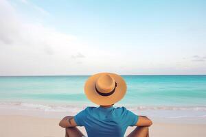 Back view of a man wearing a hat sitting on a beach. photo