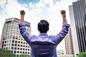 Successful businessman raising hand and expressing positivity while standing against skyscrapers background. photo