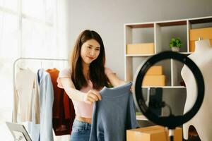 Fashion blogger concept, Young Asian women selling clothes on video streaming.Startup small business SME, using smartphone or tablet taking receive and checking photo