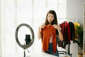 Moda blogger concepto, joven asiático mujer de venta ropa en vídeo streaming.startup pequeño negocio pequeño, utilizando teléfono inteligente o tableta tomando recibir y comprobación foto