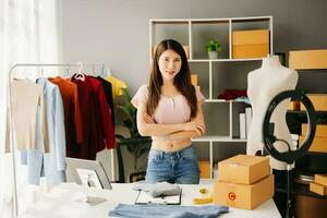 Fashion blogger concept, Young Asian women selling clothes on video streaming.Startup small business SME, using smartphone or tablet taking receive and checking photo