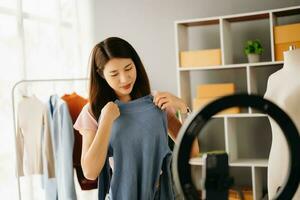 Fashion blogger concept, Young Asian women selling clothes on video streaming.Startup small business SME, using smartphone or tablet taking receive and checking photo