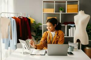 Calm curly brunette dark skinned woman on desk in office of fashion designer and holds tablet and smartphone. photo