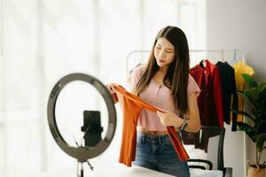 Fashion blogger concept, Young Asian women selling clothes on video streaming.Startup small business SME, using smartphone or tablet taking receive and checking photo