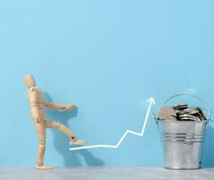A wooden mannequin and coins in a miniature bucket on a blue background, a concept of high income photo