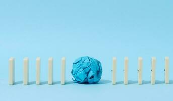 Row of dominoes and crumpled paper ball on blue background photo