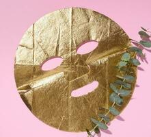 Textile cosmetic mask with gold for the face on a pink background, top view photo