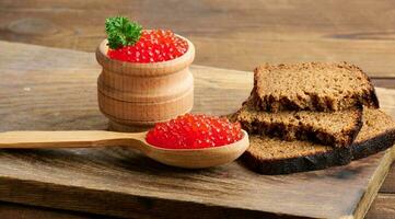 Red caviar in a wooden spoon, slices of bread on the table photo