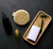 Brown glass bottle for cosmetics, a piece of soap wrapped in paper and a brush for dry body massage on a black background photo