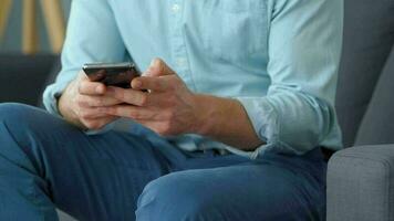 Formally dressed man sits on a sofa and enters a credit card number into a smartphone to pay online. Online shopping video