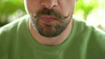 Bearded man with curled up mustache eats chocolate eclair in cafe. Close-up video