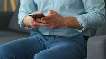 Formally dressed man sits on a sofa and enters a credit card number into a smartphone to pay online. Online shopping video