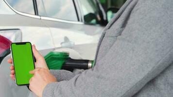 Woman uses a mobile application in a smartphone to pay for refuelling a car. Smartphone with a green screen. Chroma key video