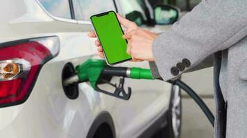 Woman uses a mobile application in a smartphone to pay for refuelling a car. Smartphone with a green screen. Chroma key video